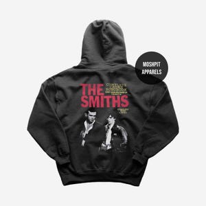 Op de afbeelding: Zwarte hoodie met een afbeelding van The Smiths. De bandnaam is rood, met de tekst "COMPLETE CHORD SONGBOOK" en "COMPLETE WITH LYRICS" op de achterkant. De hoodie heeft een "MOSHPIT APPARELS" logo.