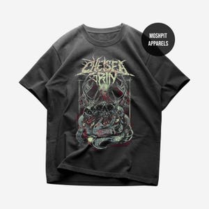 Puede incluir: Camiseta gris oscuro con un diseño gráfico que presenta el texto "Chelsea Grin" en una fuente desgastada. El diseño incluye calaveras, serpientes y otros elementos góticos. La camiseta tiene mangas cortas y cuello redondo.