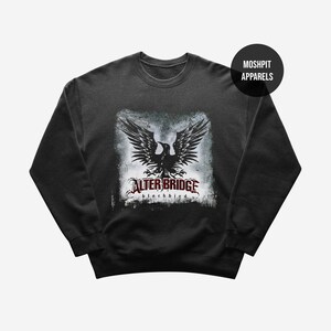 Op de afbeelding: Donkergrijze sweatshirt met een zwarte adelaar afbeelding met de tekst "ALTER BRIDGE blackbird" in rood en wit. Een zwarte cirkel met "MOSHPIT APPARELS" staat in de rechterbovenhoek.