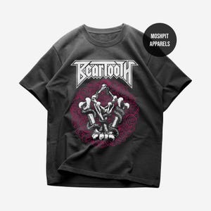 May include: Dark grey t-shirt with the band name "Beartooth" in white, above a skeleton hand design with a pink rose background. The shirt also has the text "Moshpit Apparels" on the upper right.