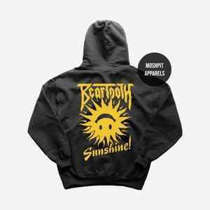 May include: A black hoodie with a yellow graphic on the back. The graphic features the word "Beartooth" above a smiling sun with the word "Sunshine!" below. The hoodie has a hood and long sleeves.