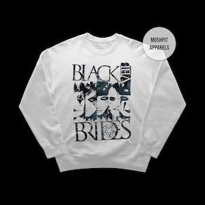 May include: White crewneck sweatshirt featuring a distressed graphic of faces and the band name "Black Veil Brides" in black. The sweatshirt has a classic fit and long sleeves. The brand name "Moshpit Apparels" is printed on a white circle.