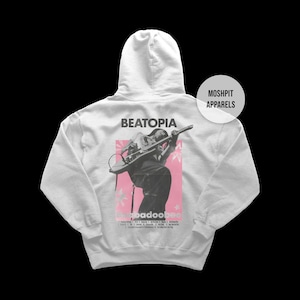 May include: A pale grey hoodie with a graphic on the back depicting a musician playing a guitar. The graphic includes the word "BEATOPIA" above the musician and the word "badoobee" below. The hoodie has a hood and a front pocket.