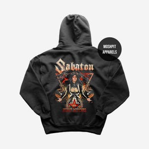 Könnte beinhalten: Dunkelgrauer Kapuzenpullover mit einem grafischen Design mit dem Wort "Sabaton" in einer stilisierten Schriftart. Das Design enthält eine Illustration einer Person und den Text "Night Witches". Der Hoodie hat eine Kapuze und eine Vordertasche.
