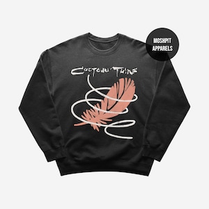 May include: Black crew neck sweatshirt with the text "Cocteau Twins" above a pink feather design and white swirls. The sweatshirt has a round neckline and long sleeves.