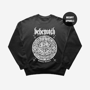 May include: Black crewneck sweatshirt with a white graphic featuring the band name "Behemoth" and a detailed circular design with the text "Polonia Heretica." The sweatshirt has a round neckline and long sleeves. The brand name "Moshpit Apparels" is in a black circle.