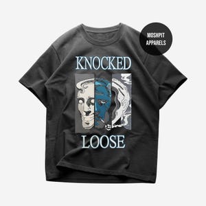 Puede incluir: Camiseta gris oscuro con un diseño gráfico con las palabras "KNOCKED LOOSE". El gráfico muestra una cara dividida en tonos azules y blancos, con un cigarrillo. La camiseta tiene cuello redondo y mangas cortas.