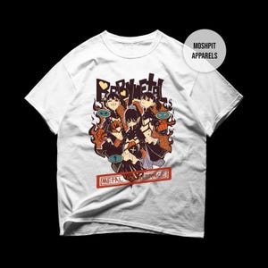 Peut inclure: T-shirt blanc avec un graphisme coloré de trois personnages de style anime et le texte "BABYMETAL". Le motif comprend des flammes et les mots "METAL RESISTANCE" dans un rectangle rouge.