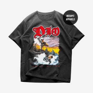May include: Dark gray t-shirt featuring a graphic of a man in water with a demon and the word "Dio" in red. The text "Holy Diver" is below the graphic. The shirt has short sleeves and a crew neck.