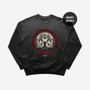 May include: Dark gray sweatshirt featuring a graphic design with two skulls, an eye, and the text "STONESOUR" in red and white. The design is set within a red circular frame. The brand name "MOSHPIT APPARELS" is printed on a black circle.