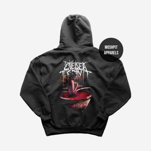 Puede incluir: Sudadera con capucha negra con un gráfico en la espalda. El gráfico presenta el nombre de la banda "Chelsea Grin" en letras góticas blancas sobre una ilustración de una persona en una bañera llena de líquido rojo. La marca "Moshpit Apparels" está en un círculo negro.
