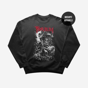 Könnte beinhalten: Dunkelgraues Sweatshirt mit einer schwarz-weißen Skelettgrafik und dem roten Wort "TRIVIUM". Das Design hat eine Used-Optik im Gothic-Stil. Das Sweatshirt hat einen Rundhalsausschnitt und lange Ärmel.
