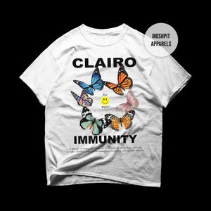 May include: White t-shirt with the word "CLAIRO" and a butterfly design. Below the butterflies is the word "IMMUNITY". The shirt also features a tracklist and the text "five music!" with a smiley face.