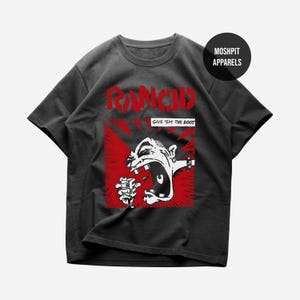 May include: Dark gray t-shirt featuring a red and white graphic. The graphic includes the band name "Rancid" in red, a screaming face, and the phrase "Give 'em the Boot". The shirt has a crew neck and short sleeves.