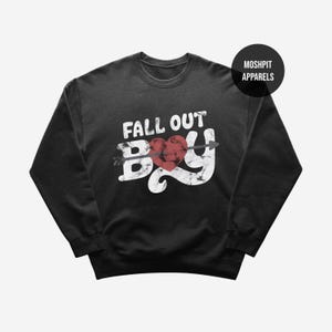 May include: Black crew neck sweatshirt featuring the text "FALL OUT BOY" in distressed white lettering. A red heart pierced by an arrow is centered within the word "BOY". The sweatshirt has a classic, casual style.