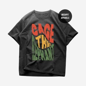 May include: Dark gray t-shirt with the text "CAGE THE ELEPHANT" in red, yellow, and green. The shirt has a crew neck and short sleeves. The brand name "MOSHPIT APPARELS" is printed on a black circle.