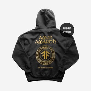 Puede incluir: Sudadera con capucha gris oscuro con un diseño dorado. El texto "AMON AMARTH" está encima de un emblema circular, con "THE PURSUIT OF VIKINGS" debajo. La sudadera tiene capucha y bolsillo delantero. La marca "MOSHPIT APPARELS" está impresa en un círculo negro.