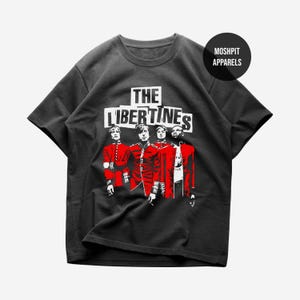 May include: Black t-shirt featuring a graphic of four figures in red coats, with the band name "The Libertines" in white block letters. A circular logo with the text "Moshpit Apparels" is in the upper right corner. The shirt is a crew neck.