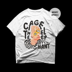 Può includere: T-shirt bianco con un design grafico raffigurante un volto stilizzato con occhi gialli e la scritta "CAGE THE EL HANT" in nero. La maglietta ha girocollo e maniche corte.