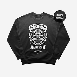 May include: Black crew neck sweatshirt with a white graphic. The graphic includes the word "BEARTOOTH" above a circular design with the letter "B" in the centre, and the word "AGGRESSIVE" below. A black circle with the text "MOSHPIT APPARELS" is in the upper right corner.
