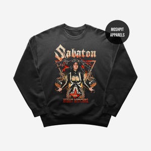 Könnte beinhalten: Dunkelgraues Sweatshirt mit einem grafischen Design mit dem Wort "Sabaton" in einer stilisierten Schriftart. Das Design umfasst eine Frau, einen roten Stern und den Text "Night Witches". Das Sweatshirt hat einen Rundhalsausschnitt und lange Ärmel.