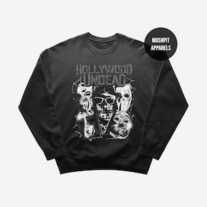 May include: Dark gray crewneck sweatshirt featuring a graphic of multiple masks and the text "Hollywood Undead". The design includes the text "Hurlie rear" on a bandana. The sweatshirt has a round neckline and long sleeves.