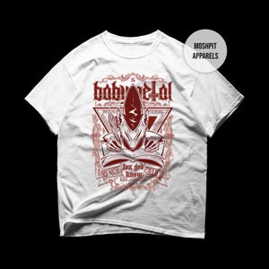 May include: White t-shirt featuring a red graphic design with the text "baby metal". The design includes an illustration of a creature reading a book, with additional text that reads "for god know". The shirt has short sleeves and a crew neck.