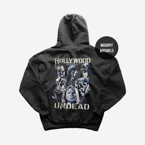 May include: Black hooded sweatshirt featuring a graphic of masked figures with the words "HOLLYWOOD UNDEAD" in white and blue. The sweatshirt has a drawstring hood and a kangaroo pocket. The brand name "MOSHPIT APPARELS" is printed on a black circle.