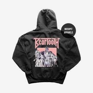 May include: Black hooded sweatshirt featuring the band name "Beartooth" in pink lettering above a silver and white graphic. The text "THE SURFACE" is below the graphic. A black circle with "MOSHPIT APPARELS" is on the upper right.