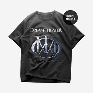 May include: Black t-shirt with the band name "Dream Theater" in white, and a silver and blue logo. The shirt has a crew neck and short sleeves. The brand name "Moshpit Apparels" is in a black circle in the upper right corner.