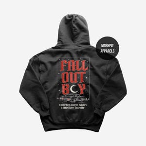 May include: Charcoal grey hoodie with a graphic on the back. The design includes the text "FALL OUT BCY" in red, a vintage car illustration, and the phrases "A Little Less Sixteen Candles, A Little More 'Touch Me'". A black circle with the text "MOSHPIT APPARELS" is on the upper right.