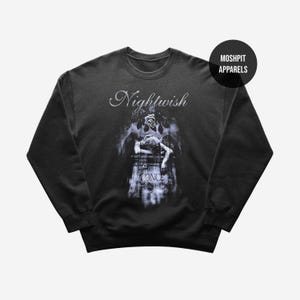 May include: Dark gray sweatshirt featuring the band name "Nightwish" in elegant script above a gothic-style graphic. The graphic depicts a figure resting on a tombstone with the word "ONCE" visible. A "Moshpit Apparels" logo is in the upper right.