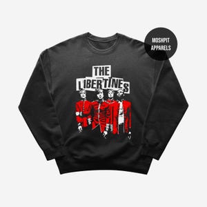 May include: Black crewneck sweatshirt featuring a graphic of four figures in red coats, with the band name "THE LIBERTINES" in white block letters. The image has a vintage, concert-style aesthetic, with a round logo in the upper right corner that says "MOSHPIT APPARELS".