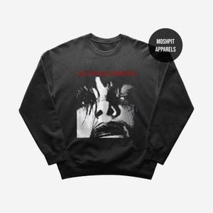 May include: Black crew neck sweatshirt with a black and white face graphic and red text reading "my bloody valentine". The brand logo "MOSHPIT APPARELS" is in a black circle in the upper right corner. A dark, moody design.