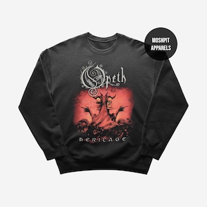 Puede incluir: Sudadera gris oscuro con el logotipo de la banda Opeth y la ilustración del álbum. El diseño incluye un fondo rojo con dos figuras y la palabra "heritage" en blanco. La marca "Moshpit Apparels" está impresa en la parte superior derecha.