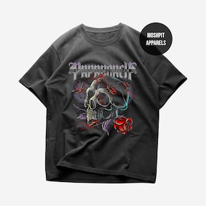 Puede incluir: Camiseta gris oscuro con un gráfico de calavera, una rosa roja y la palabra "Pappernach" en letras góticas. El diseño incluye insectos y acentos morados. La camiseta tiene cuello redondo y mangas cortas.