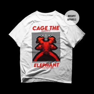Può includere: T-shirt bianca con un design grafico rosso e nero. Il design presenta le parole "CAGE THE ELEPHANT" in rosso, con un'immagine rossa e nera al centro. La maglietta ha anche il testo "MOSHPIT APPARELS" in un cerchio bianco.