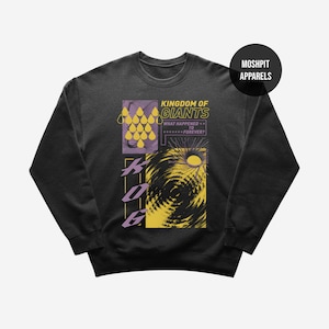 Op de afbeelding: Donkergrijze sweatshirt met een grafisch ontwerp. Het ontwerp bevat de tekst "Kingdom of Giants" en "What Happened to Forever?" in geel en wit. Er zijn ook geometrische vormen en een wervelend zonachtig beeld. De merknaam "Moshpit Apparels" is zichtbaar.