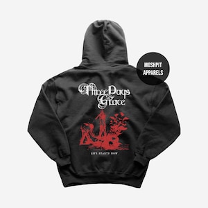 May include: Black hooded sweatshirt featuring the band name "Three Days Grace" in white script. A red graphic design and the phrase "LIFE STARTS NOW" are printed below. The sweatshirt has a hood and a "MOSHPIT APPARELS" logo.