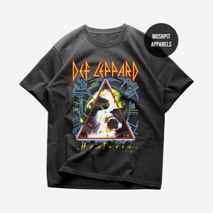 Könnte beinhalten: Dunkelgraues T-Shirt mit dem Albumcover "Hysteria" von Def Leppard. Das Design zeigt den Bandnamen in Gelb und Orange, ein dreieckiges Bild und das Wort "Hysteria" in Gelb.