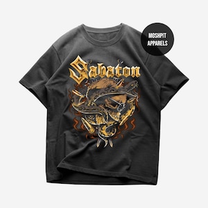 Könnte beinhalten: Dunkelgraues T-Shirt mit dem Wort "Sabaton" in goldfarbenen Buchstaben über einer Schädel- und Schlangen-Grafik. Die Grafik hat goldfarbene Akzente und Flammen. Das T-Shirt hat einen Rundhalsausschnitt und kurze Ärmel. Der Markenname "Moshpit Apparels" befindet sich in einem Kreis oben rechts.