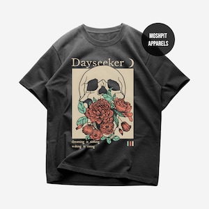 Puede incluir: Camiseta gris oscuro con un diseño de calavera y rosas rojas y rosas. La camiseta muestra la palabra "Dayseeker" y el texto "dreaming is sinking, waking is rising". También es visible el nombre de la marca "Moshpit Apparels".