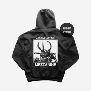 Könnte beinhalten: Schwarzer Kapuzenpullover mit einem Käfer-Grafik und dem Text "MASSIVE ATTACK" und "MEZZANINE" in einem weißen Feld. Der Pullover hat auch den Text "MOSHPIT APPARELS" in einem schwarzen Kreis.