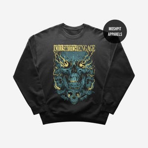 May include: Dark gray sweatshirt featuring a teal skull graphic with yellow accents and the text "KILLSWITCH ENGAGE" in yellow. The design includes flames and additional skulls. The brand name "MOSHPIT APPARELS" is in a black circle.