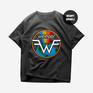 Op de afbeelding: Donkergrijs t-shirt met het logo van de band Weezer. Het logo bevat een regenboog, de naam van de band en een gestileerde "W" over een wereldbol. Het t-shirt heeft korte mouwen en een ronde hals.