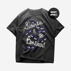 May include: Dark gray t-shirt featuring the text "Siouxsie & the Banshees" in white, with multiple purple eyes. A black circle with the text "Moshpit Apparels" is in the upper right corner.