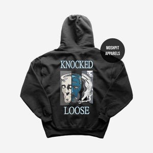 Puede incluir: Sudadera con capucha gris oscuro con un diseño gráfico que presenta tres caras estilizadas en tonos azules, blancos y grises. El texto "KNOCKED LOOSE" está arriba y abajo del gráfico. La marca "MOSHPIT APPARELS" está en la parte superior derecha.