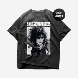 May include: Dark gray t-shirt featuring a black and white image of Siouxsie Sioux with the text "Siouxsie and the Banshees". The shirt also has the text "Moshpit Apparels" on the upper right.