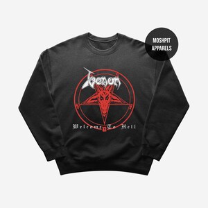 May include: Black crewneck sweatshirt featuring a red pentagram with a goat's head and the text "Venom" in white. Below the pentagram, the words "Welcome To Hell" are printed in white. The sweatshirt has a round, ribbed neckline.