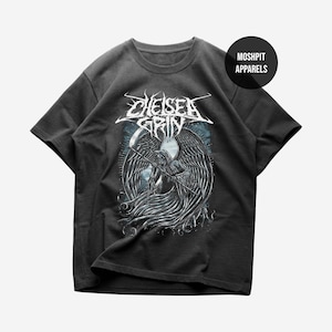 Puede incluir: Camiseta gris oscuro con un gráfico detallado de una Parca alada sosteniendo una guadaña, con el nombre de la banda "Chelsea Grin" en una fuente estilizada. La camiseta también tiene el texto "Moshpit Apparels".